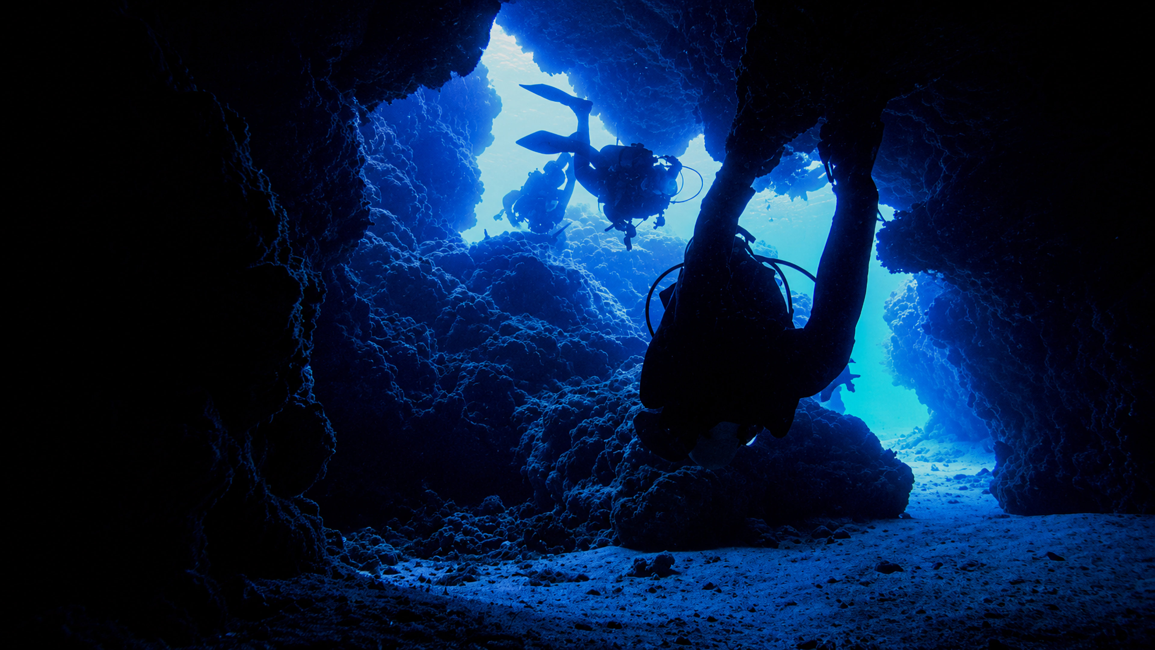 Divers silhouetted inside a Palancar canyon opening